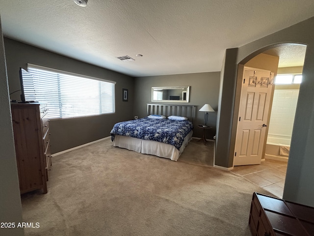 carpeted bedroom featuring a textured ceiling and ensuite bath