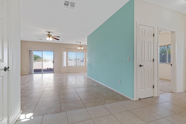 tiled empty room featuring ceiling fan with notable chandelier