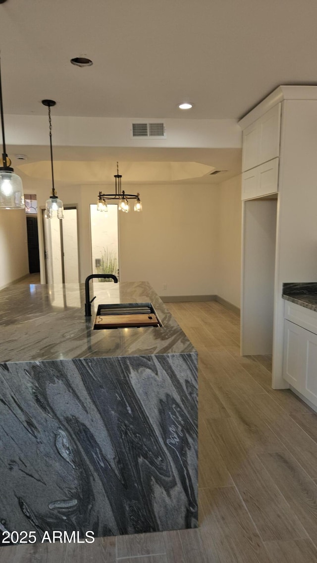 interior space featuring white cabinets, light wood-type flooring, pendant lighting, and sink