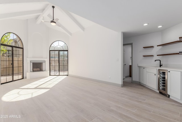 unfurnished living room featuring wet bar, wine cooler, a healthy amount of sunlight, and beam ceiling