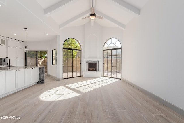 unfurnished living room featuring light hardwood / wood-style flooring, sink, ceiling fan, high vaulted ceiling, and beamed ceiling