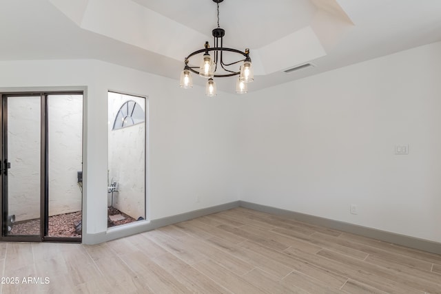 unfurnished room with a raised ceiling, light hardwood / wood-style floors, and an inviting chandelier