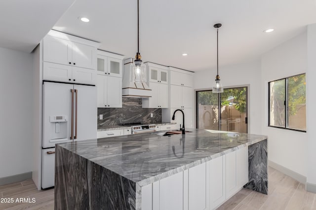 kitchen featuring a spacious island, sink, high end white refrigerator, and light stone counters