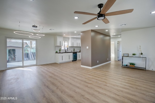 unfurnished living room featuring light wood finished floors, ceiling fan with notable chandelier, visible vents, and a sink
