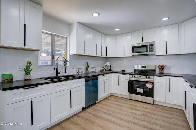 kitchen with light wood-type flooring, stainless steel appliances, a sink, dark countertops, and white cabinets