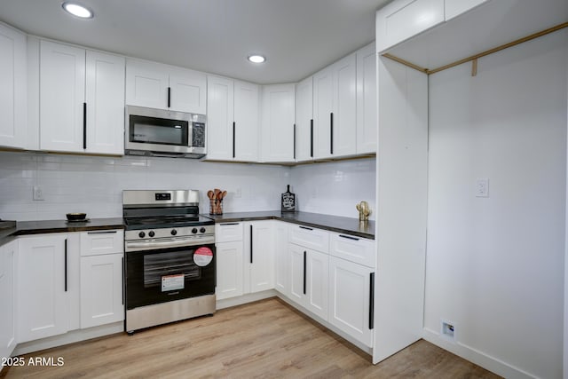 kitchen featuring white cabinetry, stainless steel appliances, dark countertops, and light wood-type flooring
