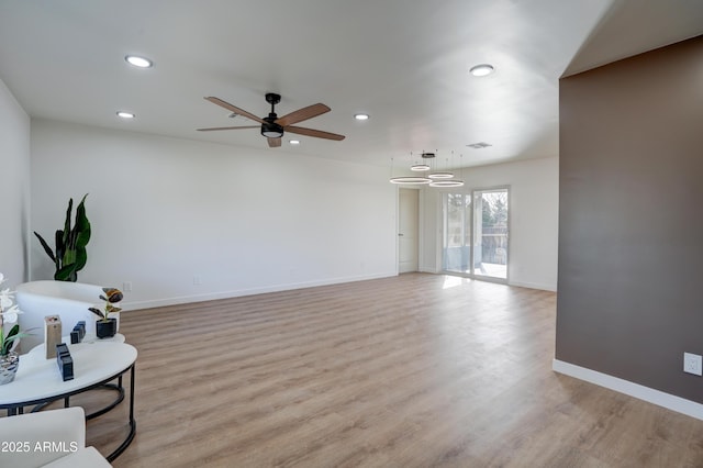 living area with light wood finished floors, ceiling fan with notable chandelier, baseboards, and recessed lighting