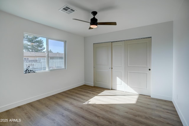 unfurnished bedroom with wood finished floors, a closet, baseboards, and visible vents
