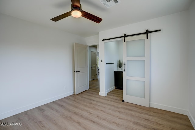 unfurnished bedroom with light wood finished floors, baseboards, visible vents, and a barn door