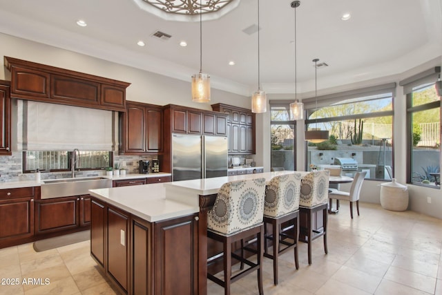 kitchen with stainless steel built in fridge, visible vents, a sink, a kitchen island, and light countertops