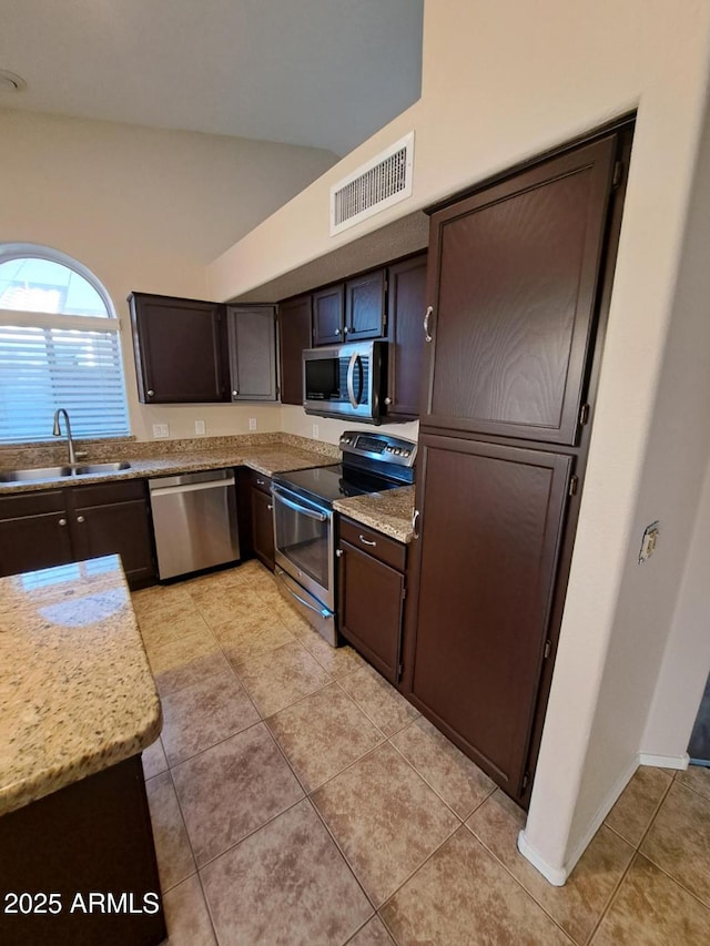 kitchen featuring light stone countertops, dark brown cabinetry, stainless steel appliances, sink, and light tile patterned floors