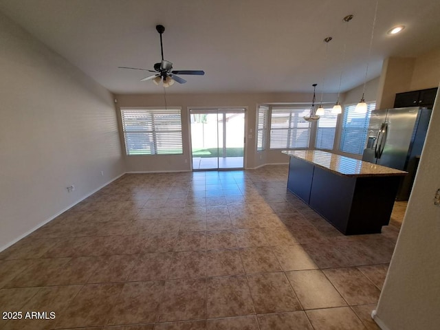 kitchen with light stone countertops, ceiling fan, decorative light fixtures, stainless steel fridge with ice dispenser, and a kitchen island