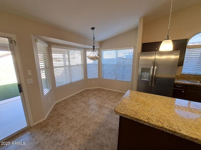 kitchen with light stone counters, decorative light fixtures, stainless steel refrigerator with ice dispenser, light tile patterned floors, and vaulted ceiling