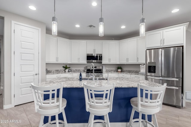 kitchen with appliances with stainless steel finishes, sink, a center island with sink, and white cabinets