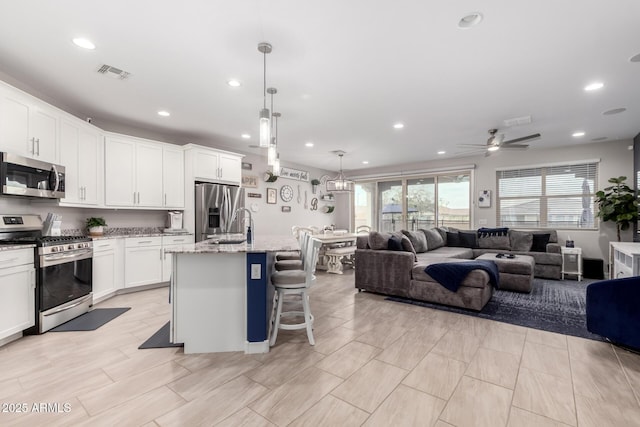 kitchen with white cabinetry, stainless steel appliances, light stone counters, a center island with sink, and decorative light fixtures