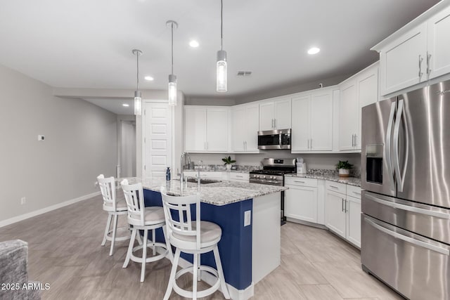 kitchen featuring sink, appliances with stainless steel finishes, white cabinetry, light stone countertops, and a center island with sink