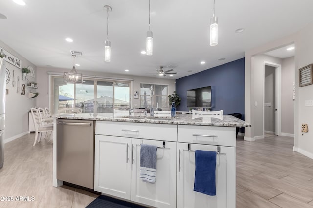 kitchen with light stone countertops, stainless steel dishwasher, an island with sink, and white cabinets