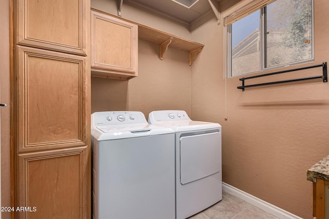 clothes washing area with washer and dryer, cabinets, and light tile patterned floors