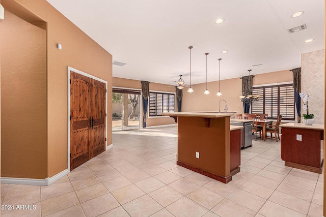 kitchen featuring a center island with sink, light tile patterned floors, pendant lighting, and stainless steel dishwasher