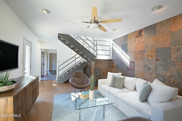 living room with ceiling fan, tile walls, and concrete floors