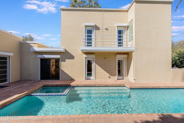 rear view of property featuring a swimming pool with hot tub and a balcony