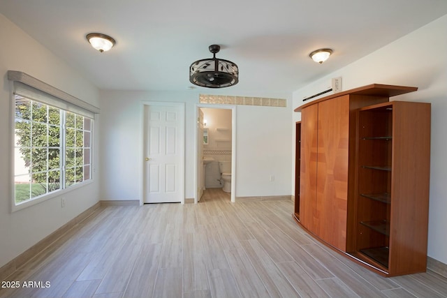 unfurnished bedroom featuring ensuite bath and light wood-type flooring