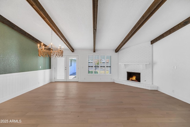 unfurnished living room featuring beam ceiling, a fireplace, a chandelier, and hardwood / wood-style flooring