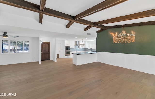 interior space with ceiling fan with notable chandelier, light hardwood / wood-style flooring, and vaulted ceiling with beams