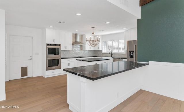 kitchen featuring kitchen peninsula, white cabinets, appliances with stainless steel finishes, and wall chimney exhaust hood