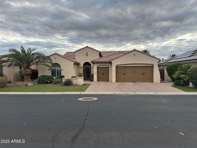 mediterranean / spanish-style house with decorative driveway, a garage, stucco siding, and a tiled roof