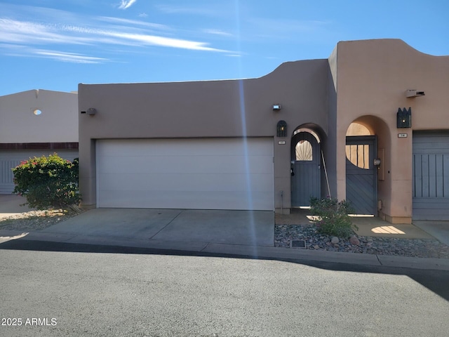 pueblo revival-style home with a garage, driveway, and stucco siding