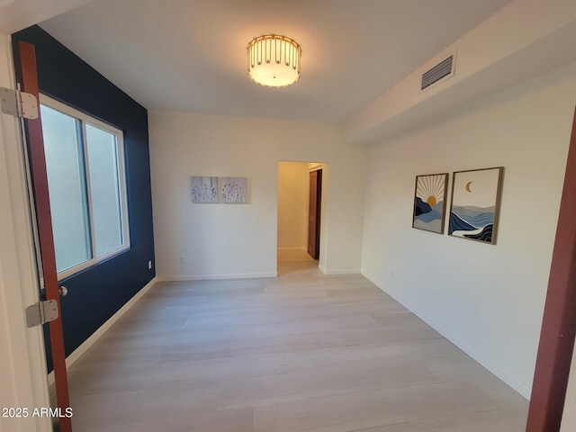 unfurnished room featuring light wood-style flooring, visible vents, and baseboards