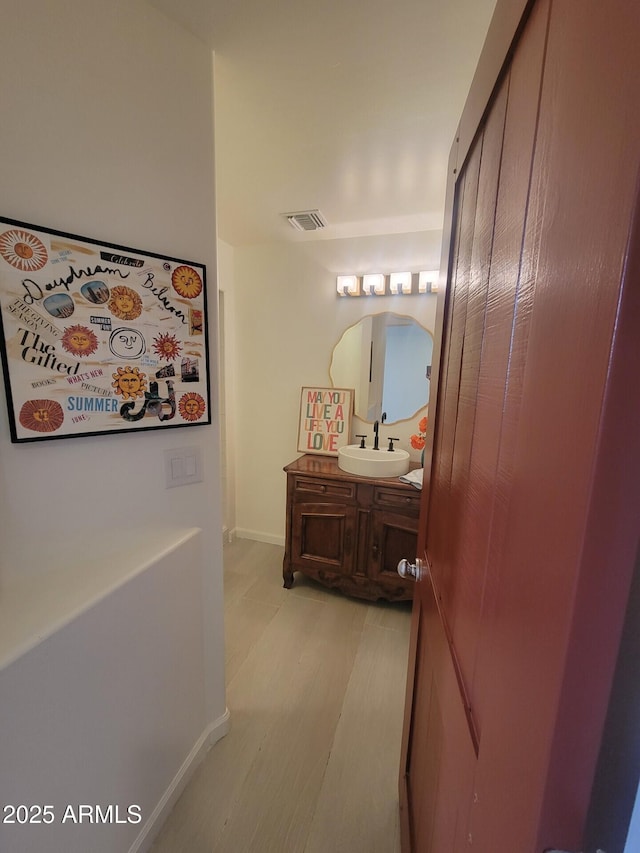 corridor with light wood-style flooring, a sink, visible vents, and baseboards