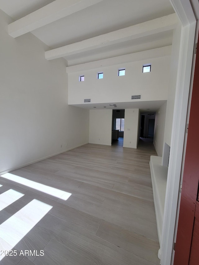 interior space featuring a towering ceiling, light wood-style flooring, visible vents, and beam ceiling