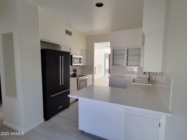 kitchen featuring a peninsula, a sink, appliances with stainless steel finishes, open shelves, and tasteful backsplash