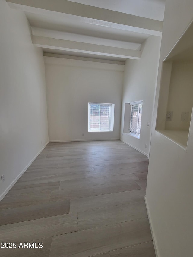 unfurnished room featuring wood finished floors, beam ceiling, and baseboards