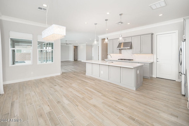 kitchen with ceiling fan, hanging light fixtures, a center island with sink, gray cabinets, and light hardwood / wood-style floors