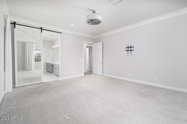 unfurnished bedroom with a barn door, ornamental molding, ensuite bath, and light colored carpet