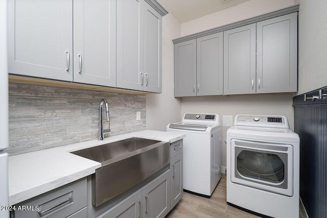 clothes washing area with washer and clothes dryer, sink, light hardwood / wood-style flooring, and cabinets