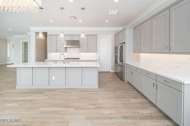 kitchen featuring backsplash, a kitchen island with sink, gray cabinets, and decorative light fixtures