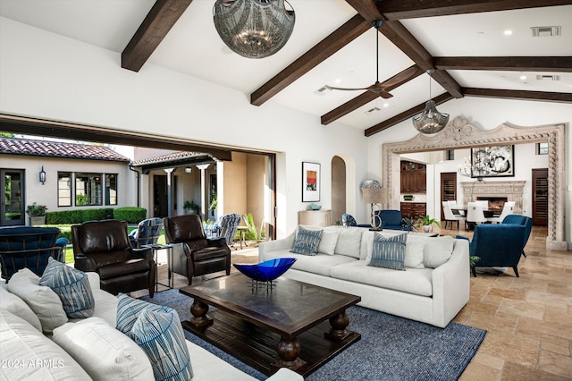 living room with ceiling fan with notable chandelier, high vaulted ceiling, beam ceiling, and a fireplace