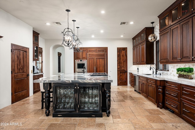 kitchen featuring light stone countertops, decorative light fixtures, a spacious island, stainless steel appliances, and sink