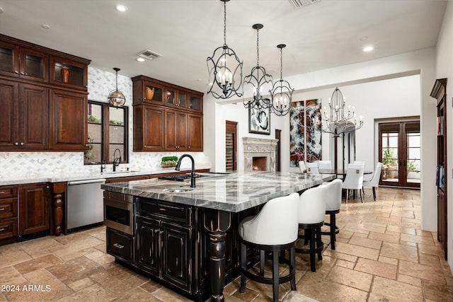 kitchen featuring an inviting chandelier, an island with sink, stainless steel appliances, decorative backsplash, and light stone counters