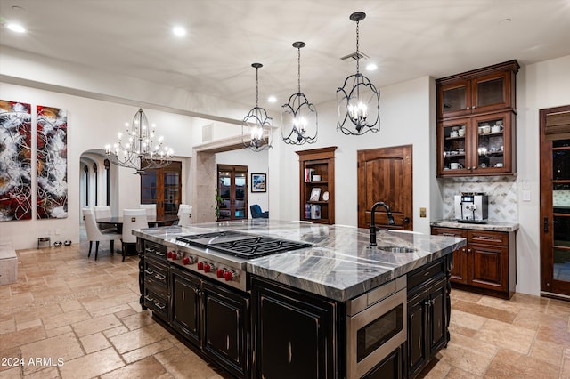 kitchen featuring sink, light stone countertops, hanging light fixtures, appliances with stainless steel finishes, and a center island with sink