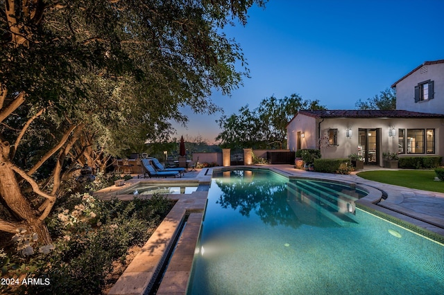 pool at dusk with an in ground hot tub and a patio