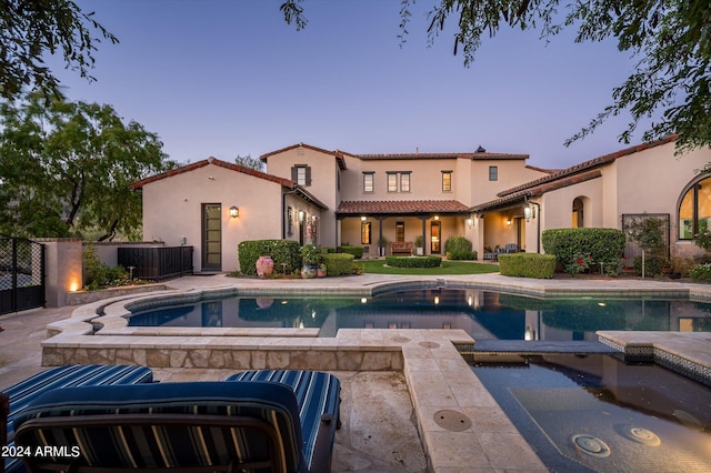 pool at dusk with an in ground hot tub, central air condition unit, and a patio area