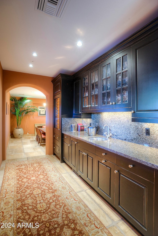 bar featuring backsplash, light stone countertops, sink, and dark brown cabinetry