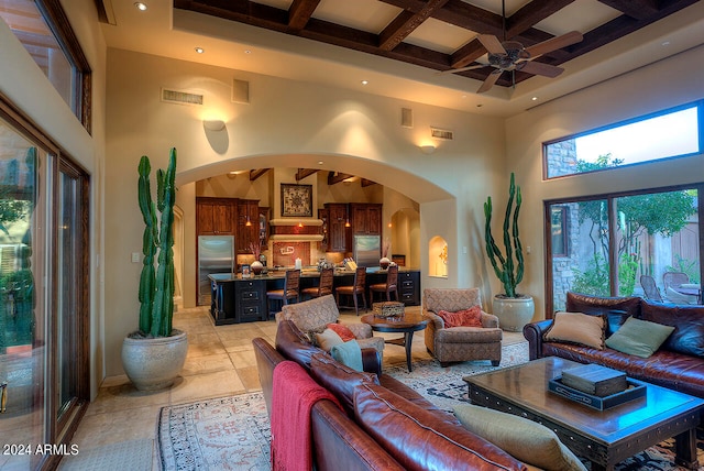 living room with ceiling fan, beamed ceiling, a high ceiling, and coffered ceiling