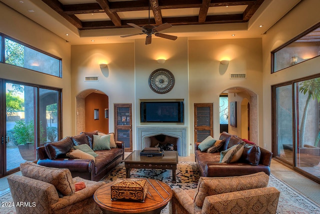 living room featuring ceiling fan, a towering ceiling, beamed ceiling, and coffered ceiling