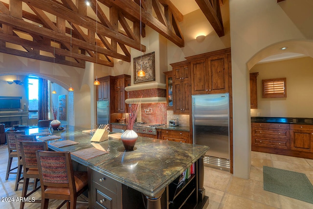 kitchen with stainless steel built in fridge, tasteful backsplash, high vaulted ceiling, a center island with sink, and beam ceiling